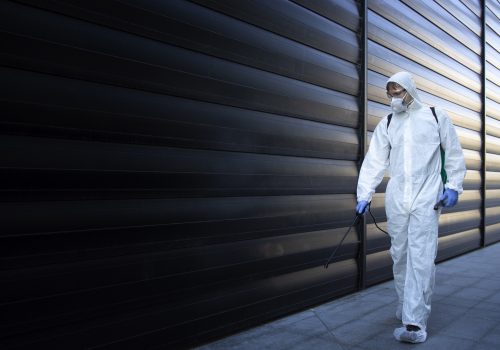 Person in white chemical protection suit doing disinfection and pest control and spraying poison to kill insects and rodents.